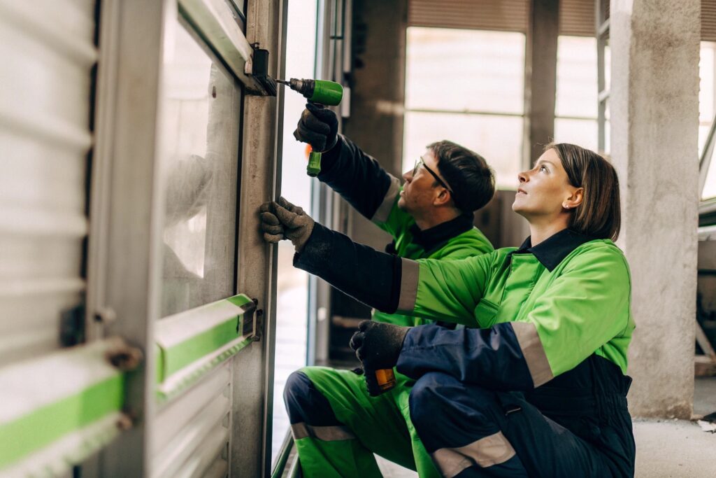 Zwei Fachkräfte bei der Wartung einer Brandschutztür in einem Industriegebäude – regelmäßige Inspektion zur Sicherstellung der Funktion im Brandfall.