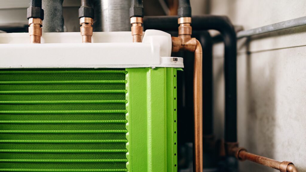 Nahaufnahme eines modernen Wärmetauschers mit grünem Gehäuse und Kupferrohren – sichtbar sind Kühlrippen und Rohrleitungen, die den Wärmeübertragungsprozess veranschaulichen.